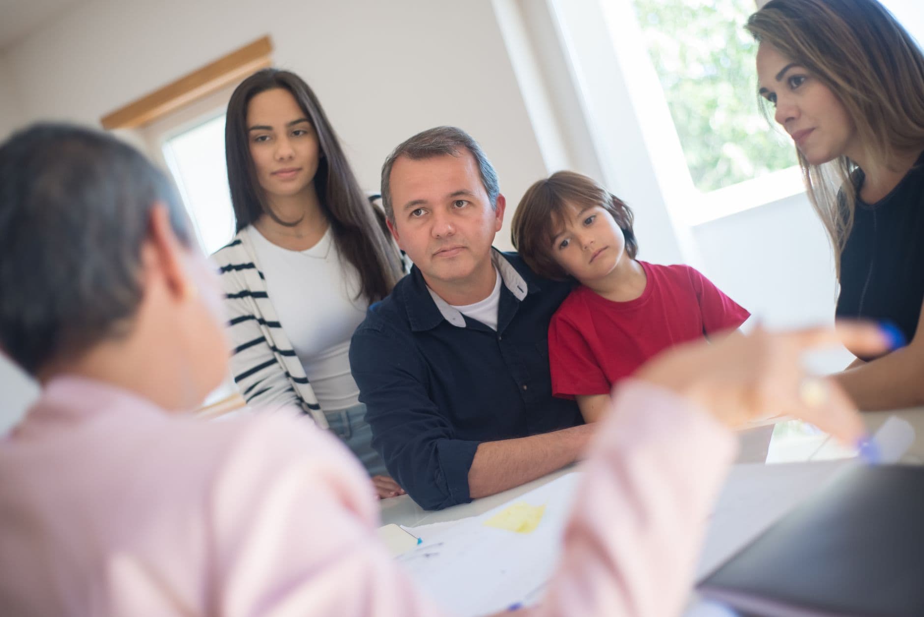 Une famille est assise et écoutée par une personne hors champ dans un intérieur lumineux.